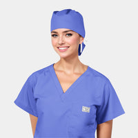 A person wearing a periwinkle blue scrub hat with a matching scrub top. The hat has a small pouch and a ribbon tie at the back.