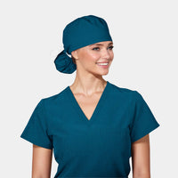 A person wearing a Caribbean Blue ponytail scrub hat with a matching scrub top, against a white background.