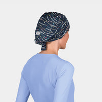 woman wearing a navy scrub cap with friendship bracelets on it and a light blue scrub top on a white background