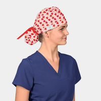 Person wearing a blue scrub top and a patterned scrub cap with red hearts on a light gray background