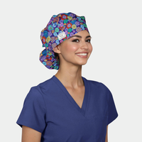 Woman wearing a colorful floral bouffant scrub cap and blue scrub top on a white background