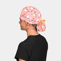 woman wearing a black scrub top and a pink ponytail halloween scrub cap that has skeletons, ghosts and pumpkins
