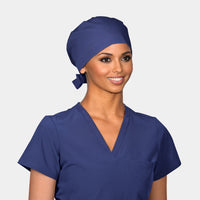 A person wearing a dark navy blue pixie scrub hat with a tie at the neck, matching the hat with a navy blue scrub set.
