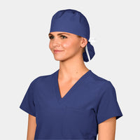 A person wearing a dark navy blue ponytail scrub hat and matching v-neck scrub set on a light grey background