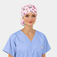 Person wearing a light blue scrub top and a pink scrub cap with dogs on it on a plain background