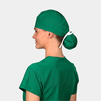 A person wearing a Pine Green solid color ponytail scrub hat and matching surgical scrubs.
