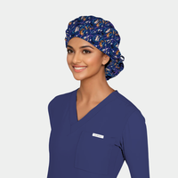 Woman wearing a blue scrub top and a scrub cap with cats on it.on a light gray background