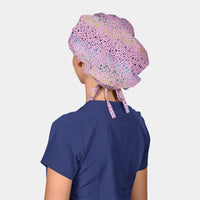 woman wearing a navy blue scrub top and a pink bouffant scrub cap with stars all over it on a white background