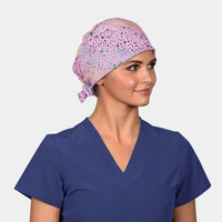 Woman wearing a blue scrub top and a pink scrub cap with stars on it on a white background