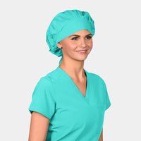 woman wearing a green bouffant surgical cap and a green scrub top on a light grey background.