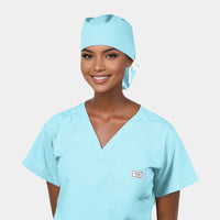 A person wearing a light blue V-neck scrub suit and a matching light blue ponytail surgical hat on a light grey background.