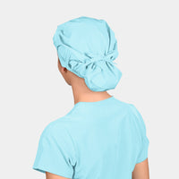 woman wearing a turquoise surgical cap and a turquoise scrub top on a light grey background