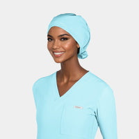 A person wearing a turquoise blue pixie scrub hat and a matching surgical scrub uniform.