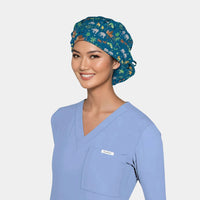 Woman wearing a blue scrub top and Noah's Ark themed scrub cap on a white background