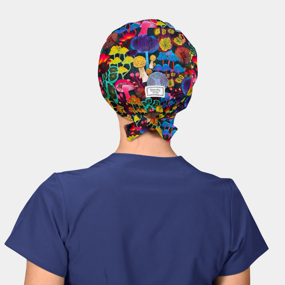 woman wearing a navy blue scrub top and a scrub hat that has brightly colored mushroms