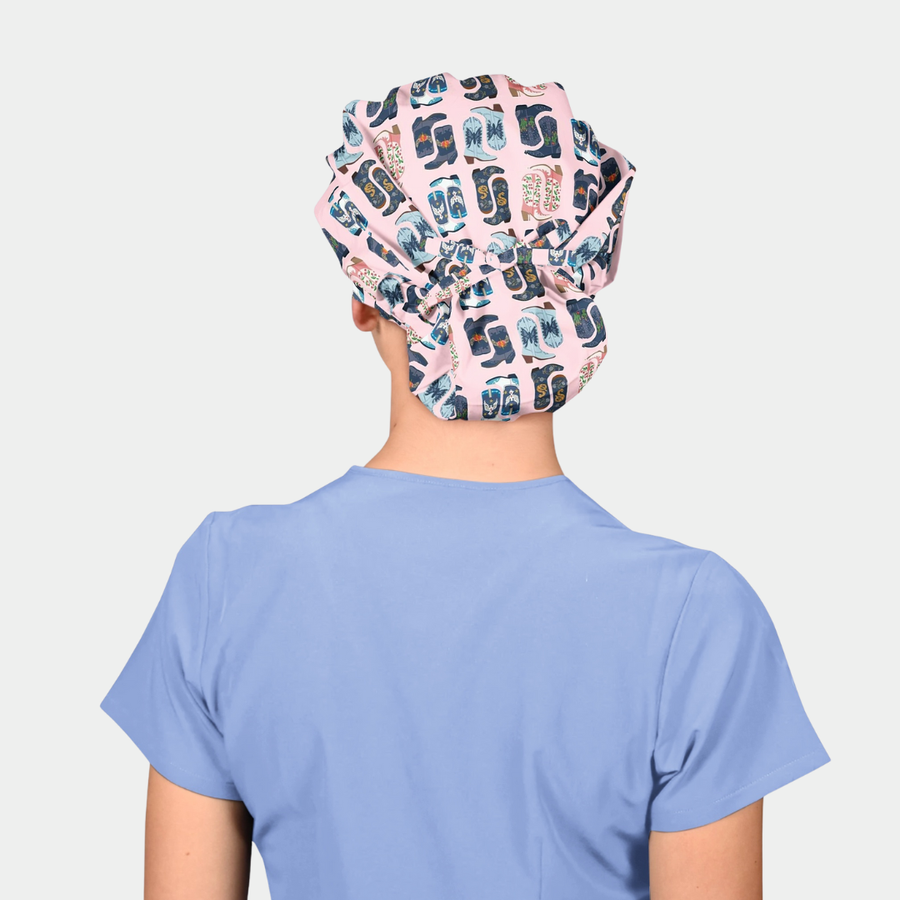 woman wearing a light blue scrub top and a bouffant scrub hat that is light pink with blue cowboy boots on it