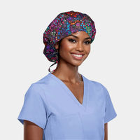 woman wearing a bouffant scrub cap that has colorful circles on it and a light blue scrub top on a white background.