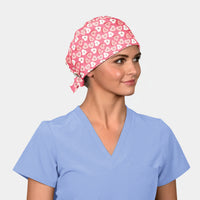 Person wearing a pink scrub cap with heart pattern and a light blue scrub top on a plain background