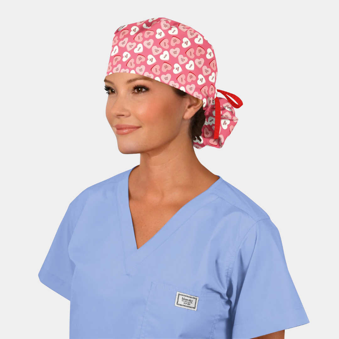 Woman wearing a light blue scrub top and a pink scrub cap with heart pattern on a white background