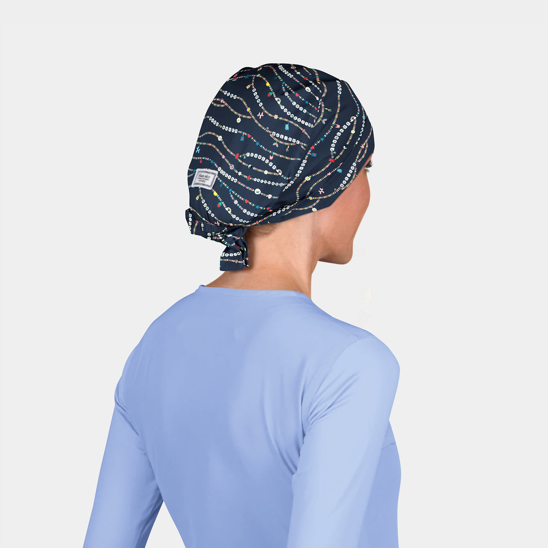 woman wearing a navy scrub cap with friendship bracelets on it and a light blue scrub top on a white background