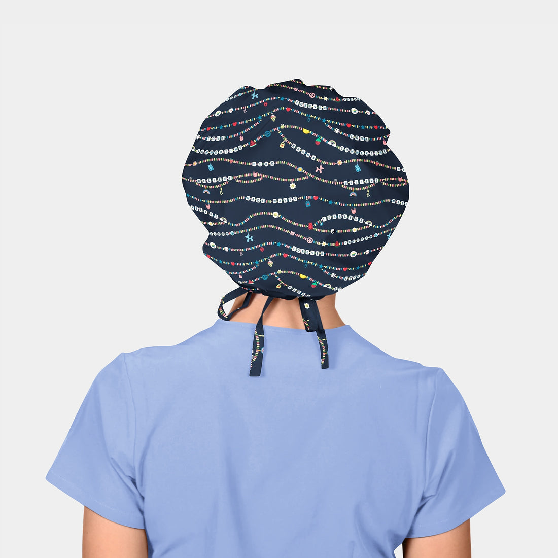 woman weating a navy scrub hat with friendship bracelets on it and a light blue scrub top on a white background