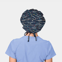 woman weating a navy scrub hat with friendship bracelets on it and a light blue scrub top on a white background