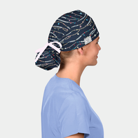 Person wearing a navy scrub cap with friendship bracelets on it and a light blue scrub top on a white background