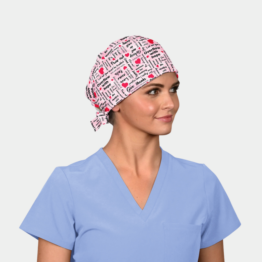 woman wearing a breast cancer themed scrub hat that is pink with black words and red hearts on it