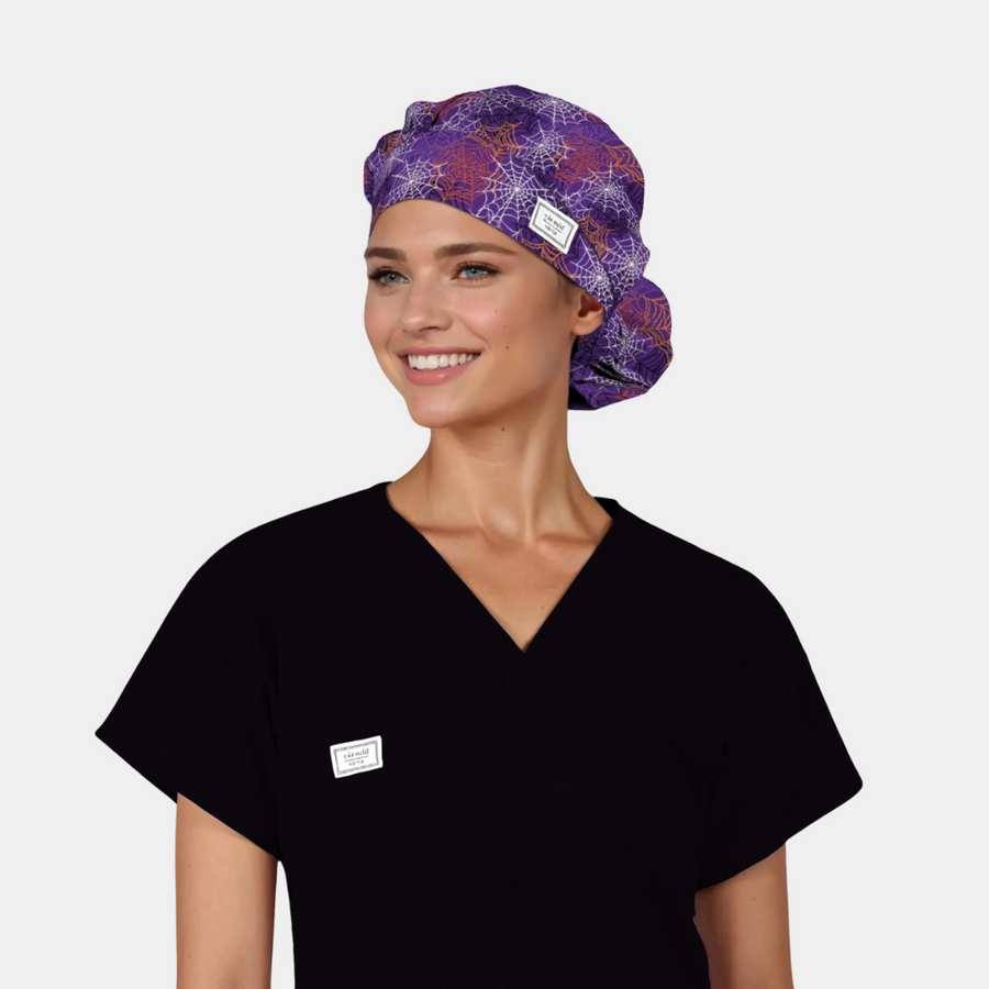 person wearing a black scrub top with a halloween scrub hat that is purple with white, orange and pink spider webs