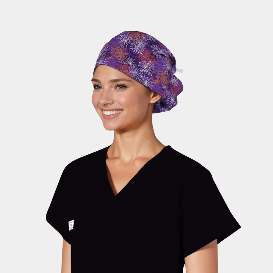 woman wearing black scrubs and a purple halloween hat with white, orange and pink spiderwebs on it