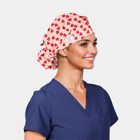 Person wearing a blue scrub top and a patterned scrub cap with red hearts on a light gray background