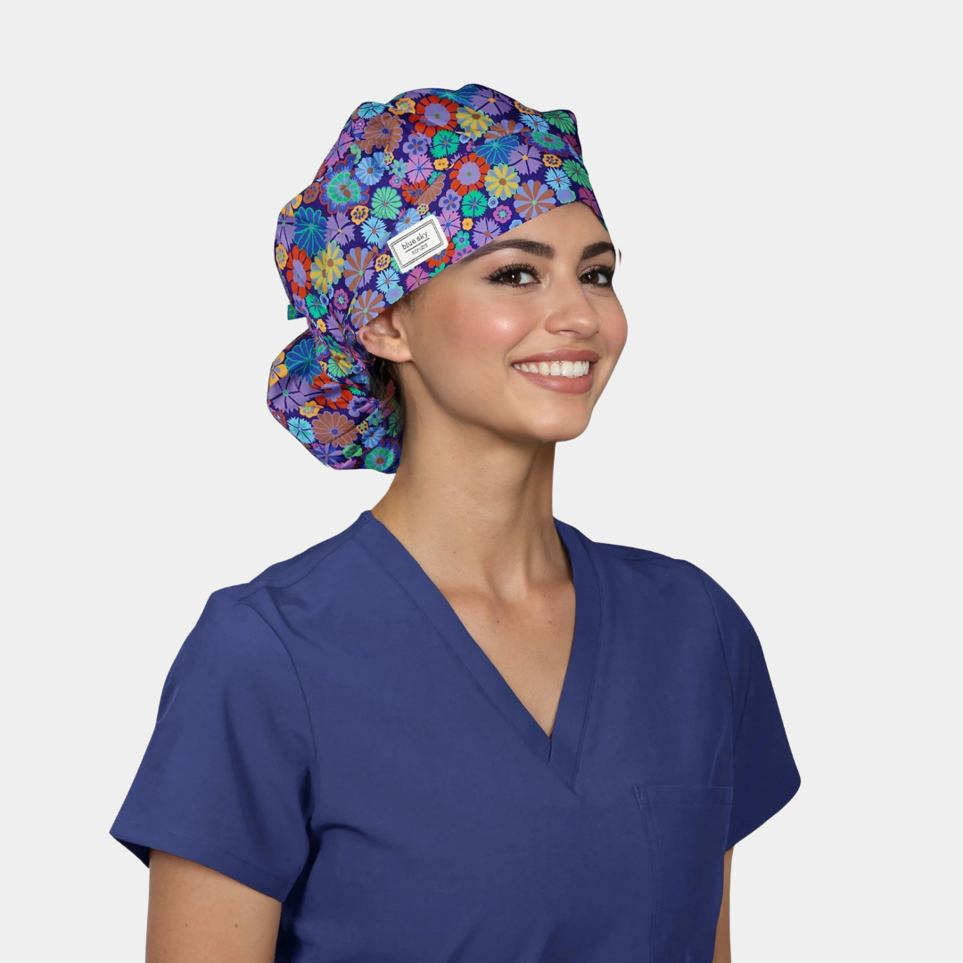 Woman wearing a colorful floral bouffant scrub cap and blue scrub top on a white background