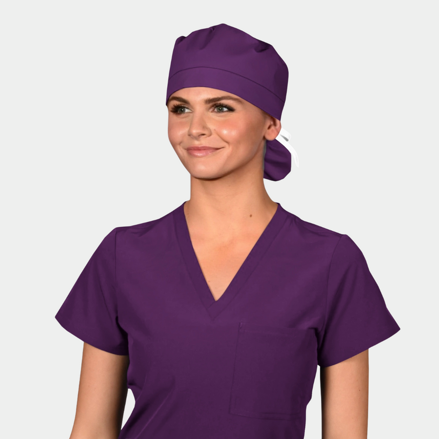 Person wearing a purple scrub top and matching purple ponytail scrub hat on a white background