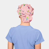 woman wearing a light blue scrub top and a pink bouffant scrub hat that has trees and animals on it