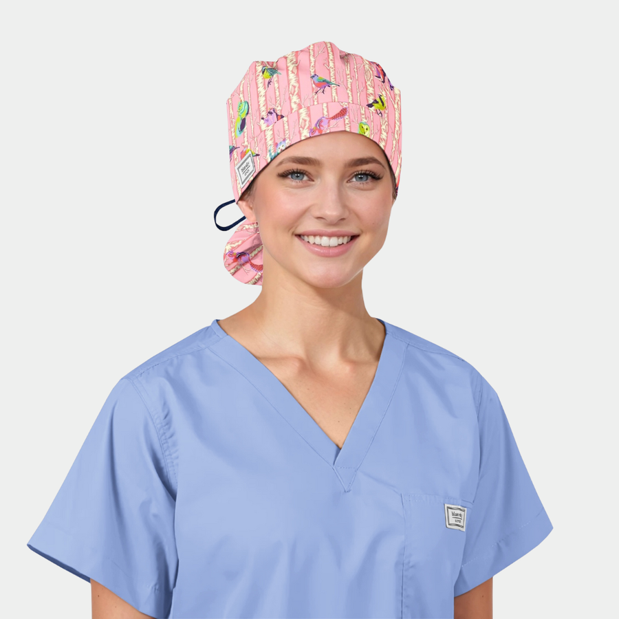 girl wearing a light blue scrub top and a pink ponytail scrub hat with birds and monkeys on it