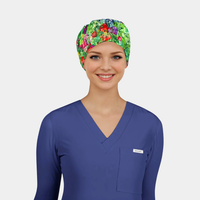 Woman wearing a blue scrub top and colorful scrub hat with vegetables on it on a light gray background