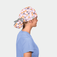 woman wearing a light blue scrub top and a ponytail scrub hat that is pink with cats on it