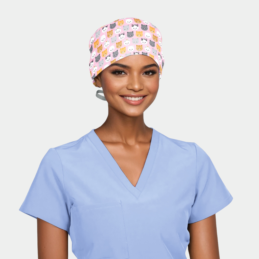 person wearing a light blue scrub top and a pink scrub hat with cute cats on it