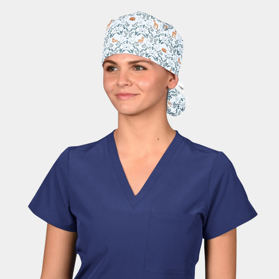 woman wearing a navy blue scrub top and a ponytail scrub cap with deer and blue vines on a light blue background