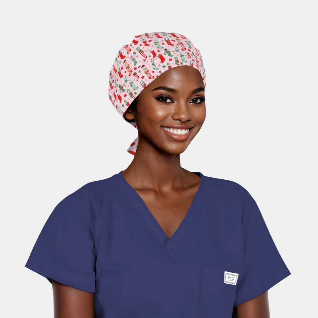 woman wearing a navy scrub top and a christmas scrub hat that is pink with stocking and dogs on a white background.