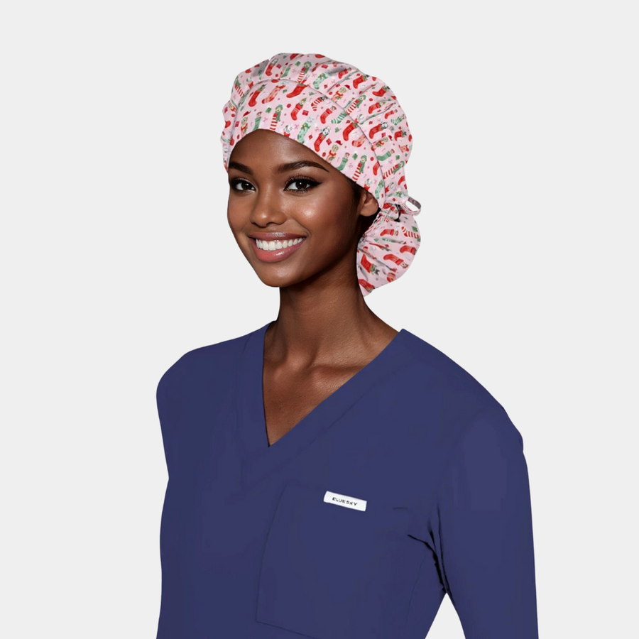 Woman wearing a blue scrub top and christmas scrub cap on a plain background