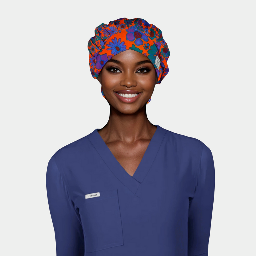 woman wearing a navy blue scrub top with a bouffant style scrub hat on that is bright orange with big blue and green flowers