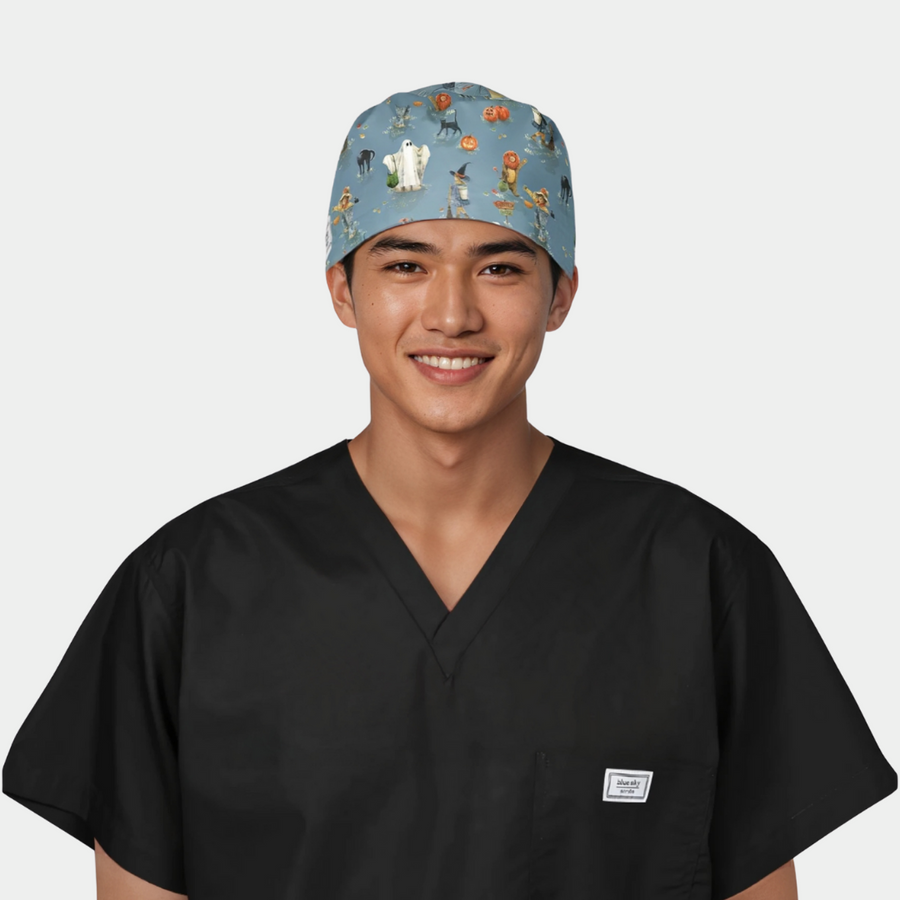 man wearing a black scrub top with a halloween scrub hat that has ghost, pumpkins and cats on a blue background