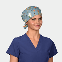 woman wearing a navy blue scrub top and a halloween scrub hat that has ghosts, pumpkins and cats on a medium blue background