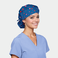 Woman wearing a blue scrub cap with red heart patterns and a matching scrub top on a light gray background