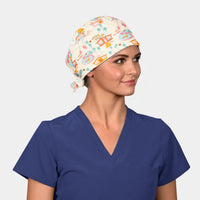 woman wearing a navy scrub top and a scrub cap that is cream with pastel scenes of houses and palm trees