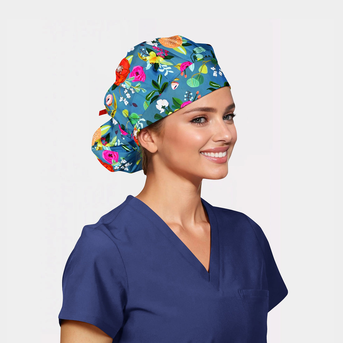 Woman wearing a colorful floral bouffant scrub cap and navy scrubs on a light gray background