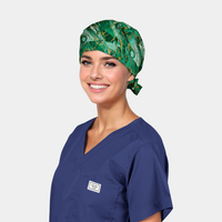 Person wearing a green patterned scrub cap and blue scrub top on a light gray background