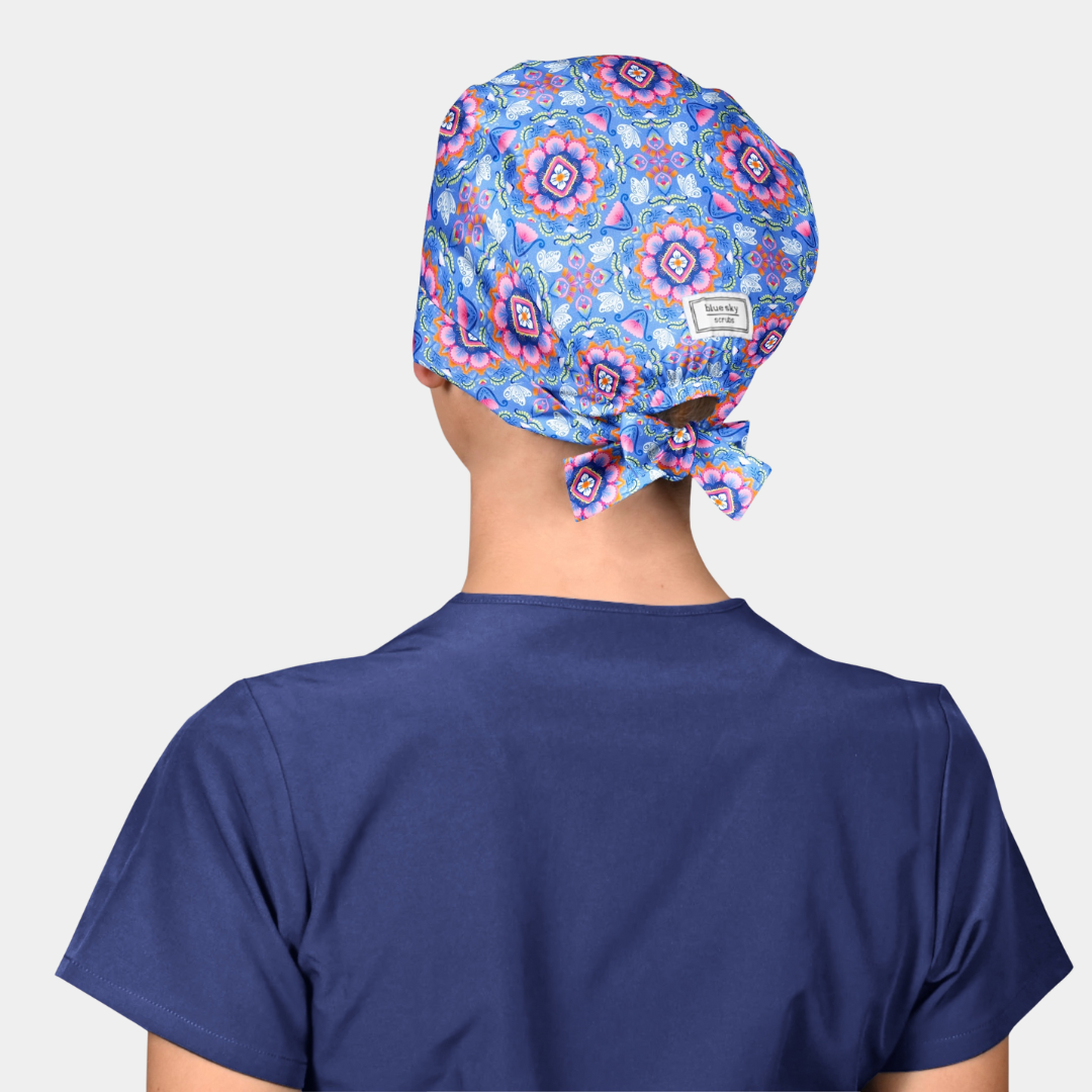 woman wearing a pink and blue scrub hat and a navy blue scrub top on a white background