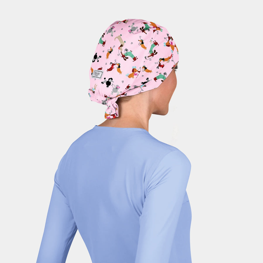 woman in a light blue scrub top and a scrub hat that is pink with dogs on it on a white background